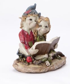 two Cornish piskies sitting close together as they read from a book. Both piskies have cheerful expressions, highlighting their enjoyment of the moment.