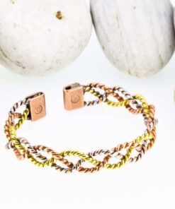 Open magnetic copper therapy bangle with twisted copper, brass, and silver-tone wires in an interlinked design, featuring rectangular magnetic ends, displayed against smooth white pebbles.