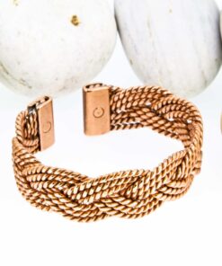 Thick braided magnetic copper therapy bangle with multiple twisted copper strands woven together, finished with rectangular magnetic ends, displayed against smooth white pebbles.