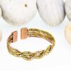 Twisted rope-design magnetic copper therapy bangle with intertwined copper, brass, and silver-tone strands, featuring rectangular magnetic ends, displayed against smooth white pebbles.
