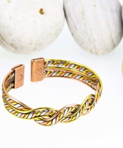 Twisted rope-design magnetic copper therapy bangle with intertwined copper, brass, and silver-tone strands, featuring rectangular magnetic ends, displayed against smooth white pebbles.