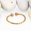 Slim twisted magnetic copper therapy bangle with intertwined copper and brass strands, finished with round magnetic ball ends, displayed against smooth white pebbles.