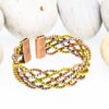 Multi-strand magnetic copper therapy bangle featuring twisted copper, brass, and silver-tone wires, with two rectangular magnetic ends, displayed against smooth white pebbles.