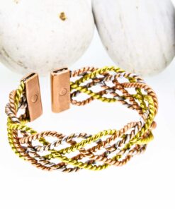 Multi-strand magnetic copper therapy bangle featuring twisted copper, brass, and silver-tone wires, with two rectangular magnetic ends, displayed against smooth white pebbles.