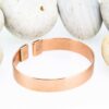 Plain polished magnetic copper therapy bangle with a smooth wide band and rectangular magnetic ends, displayed against a backdrop of smooth white pebbles.