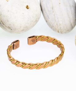Twisted two-tone magnetic copper therapy bangle with a copper and brass spiral design, finished with rectangular magnetic ends, displayed against smooth white pebbles.