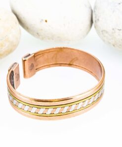 Wide magnetic copper therapy bangle with a central silver-tone braided inlay bordered by smooth brass accents, finished with rectangular magnetic ends, displayed against smooth white pebbles.