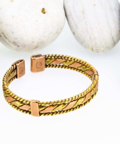 Magnetic copper therapy bracelet in an open cuff design, featuring alternating copper and brass diagonal panels bordered by twisted rope edges, with magnets set at each end for potential arthritis relief, improved blood flow, and overall wellness, displayed against smooth white pebbles.