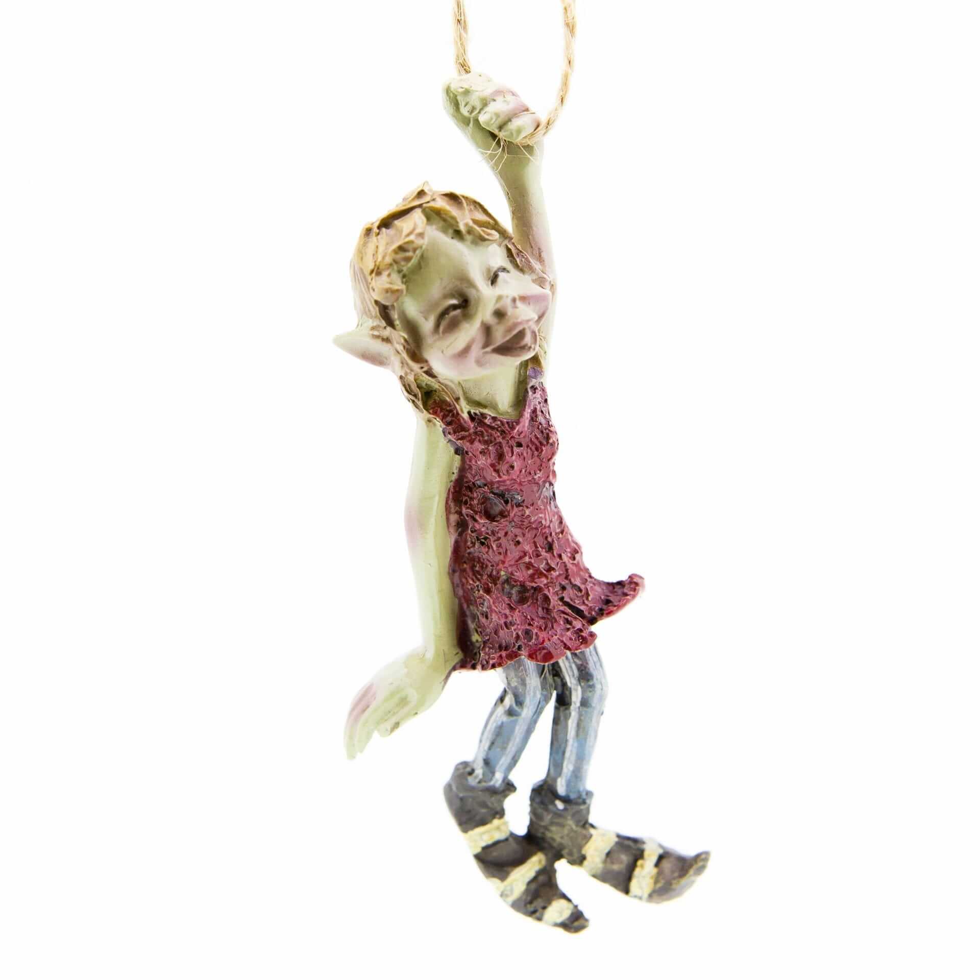A playful Pesky Pisky character hanging in a joyful pose. The figure wears a vibrant red dress and colorful striped boots, with a mix of textures and colors