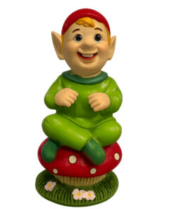 Cheerful green‑clad Cornish piskey figurine sitting cross‑legged on a red spotted mushroom with flowers at the base.