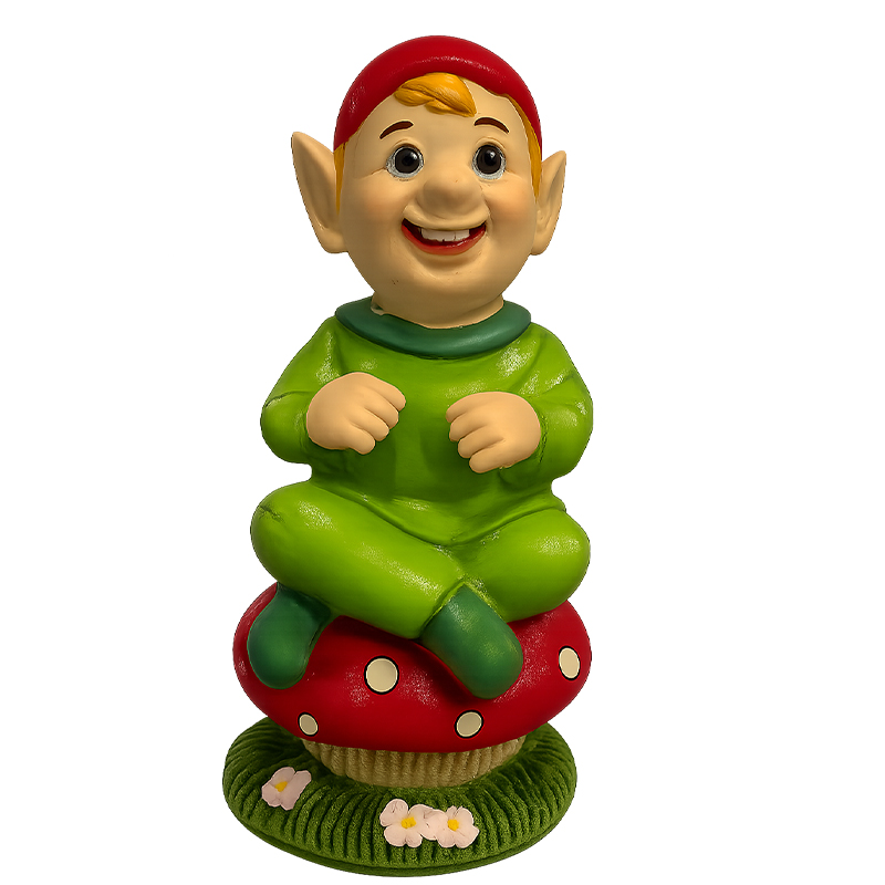 Cheerful green‑clad Cornish piskey figurine sitting cross‑legged on a red spotted mushroom with flowers at the base.