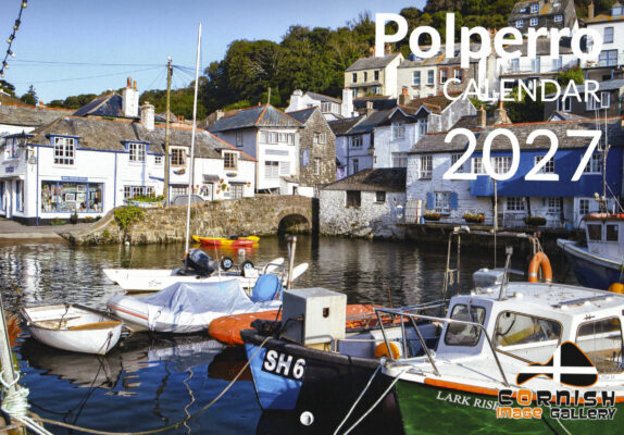 A harbor scene in Polperro, Cornwall, featuring small boats moored in calm water in the foreground, including a green and white boat labeled "LARK RISE". Whitewashed stone cottages with slate roofs line the harbor and rise up a green hillside under a blue sky. Polperro 2027 calendar