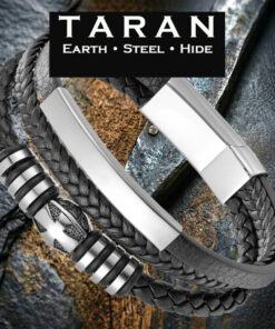 A Taran men's black leather multi-strand bracelet showing three distinct layers permanently attached to a wide, satin-polished silver stainless steel magnetic slide clasp. The top strand is a wide, flat band of genuine black pebbled leather topped with a long, curved, polished silver stainless steel ID bar. The middle strand is a rounded black leather braid threaded with a central silver shield bead featuring an embossed cross crest, flanked by ribbed silver spacer rings and dark bands. The bottom strand is a tight, high-density braided leather plait in a herringbone pattern.