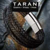 A Taran men's black braided leather multi-strand bracelet featuring a heavy triple-strand layout. Three thick rows of tightly woven black leather hide run parallel to each other, creating a dense, tactile herringbone texture. The strands connect into a large, curved, mirror-polished silver stainless steel magnetic slide clasp.