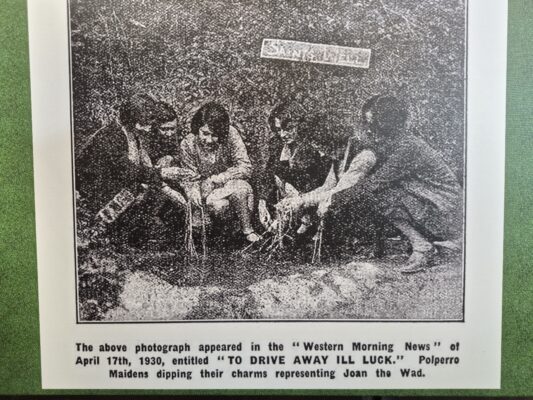Archival newspaper photograph from April 17, 1930, titled "To Drive Away Ill Luck," showing young Polperro maidens kneeling around Saints' Well to submerge their Joan the Wad charms in water.