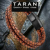 Men's TARAN double-strand cognac brown braided leather bracelet with two-tone weathered hide and a brushed black magnetic steel clasp, displayed on a dark slate and wood background.